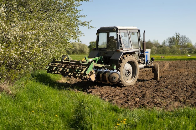 Der Traktor fährt über das Feld und bearbeitet das Land. Landwirtschaftsfahrzeuge arbeiten auf dem Land. Die Aussaat ist der Prozess des Einpflanzens von Samen in den Boden als Teil der zeitigen Frühlingszeit