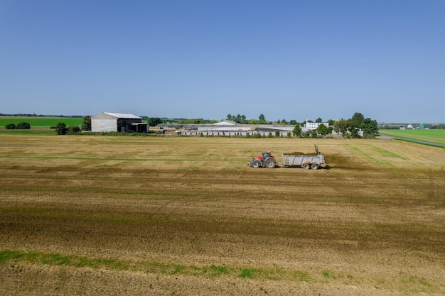 Der Traktor verstreut Mist auf dem Feld. Füttern des Bodens vor dem Eggen. Sicht von oben. Landwirtschaftliche Arbeit.