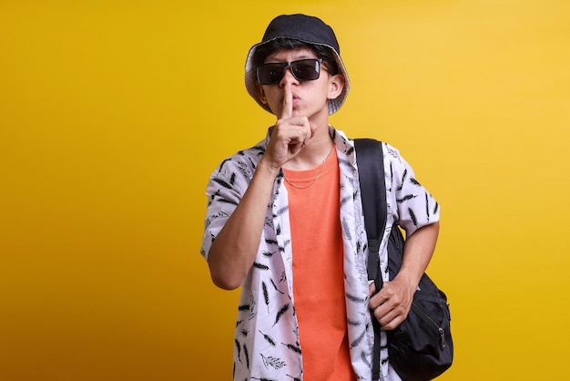 Der trendige junge Mann mit Sonnenbrille und Rucksack legt seinen Zeigefinger an sein Handgelenk