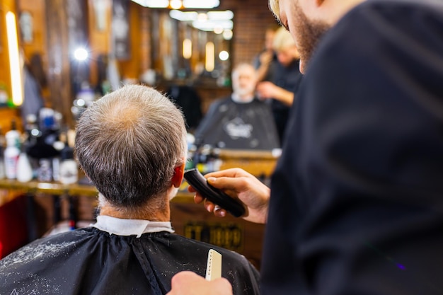 Der trendige, stilvolle Meister schneidet die Haare des alten Kunden im modernen Friseursalon