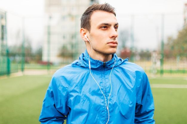 Der Typ hört während des Trainings Musik. Ein junger Mann treibt Sport, rennt auf dem Fußballplatz. Der Typ arbeitet an der frischen Luft.