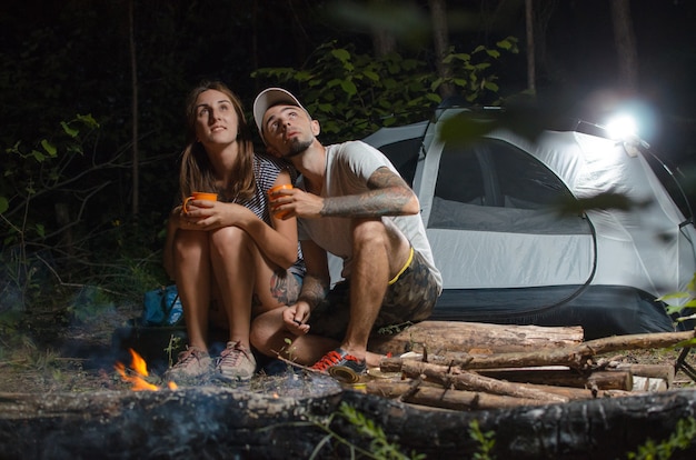 Foto der typ mit dem mädchen im wald mit einem zelt in der nacht, am lagerfeuer sitzend