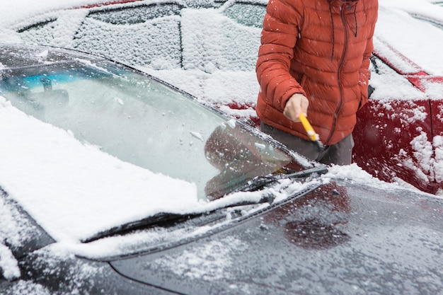 Der Typ reinigt das Auto mit einer Bürste vom Schnee, Schlechtes Schneewetterkonzept