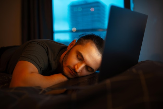Der Typ schläft im Bett, während er im Laptop zu Hause arbeitet
