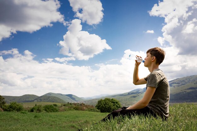 Foto der typ sitzt auf einem berg und trinkt wasser aus einer flasche schöne berglandschaft und sonniger tag