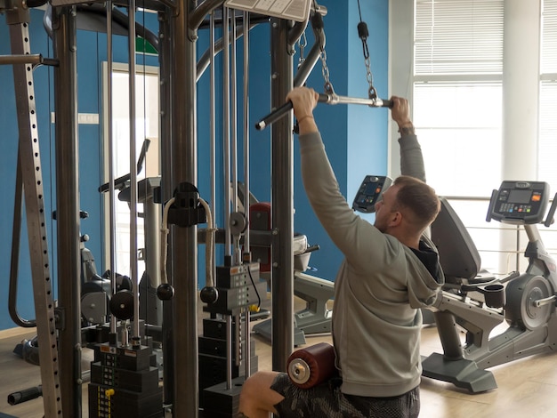 Der Typ treibt Sport auf einem Simulator in einem Fitnessclub, der Typ pumpt Muskeln