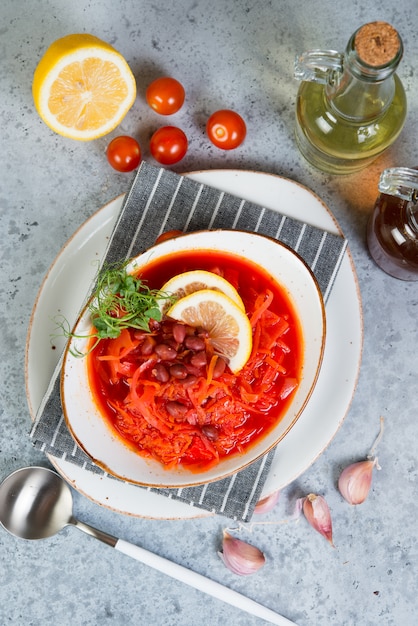 Der ukrainische vegetarische Borschtsch mit roten Bohnen in einer weißen Platte steht auf einem grauen Betonhintergrund. Draufsicht