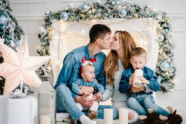 Der Vater, die Mutter umarmen den kleinen Sohn und die Tochter in der Nähe des Weihnachtsbaums