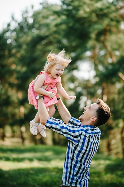 Der Vater kotzt und spinnt die Tochter im Sommerurlaub in der Natur. Papa und Mädchen spielen bei Sonnenuntergang im Park. Mädchenfliegen. Konzept der freundlichen Familie. Nahaufnahme.