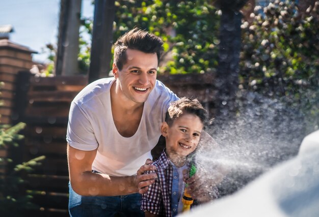 Der vater und der sohn putzen ein auto mit einem schlauch