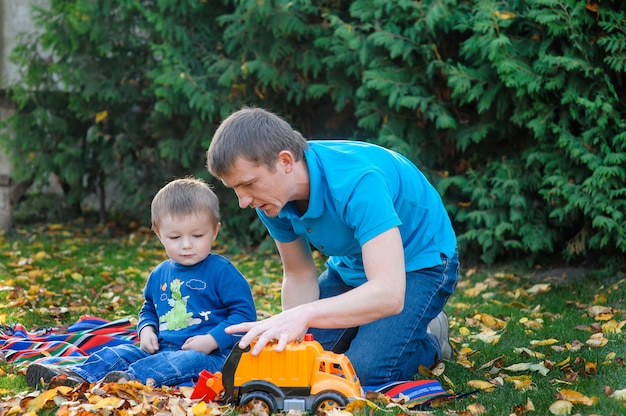 Der Vater und Sohn, die im Park spielen, spielen Auto in einem Park auf dem Gras im Herbst