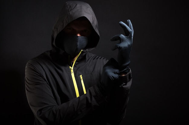 Der Verbrecher in der Maske zieht einen Handschuh an. Vorbereitung auf Raub.