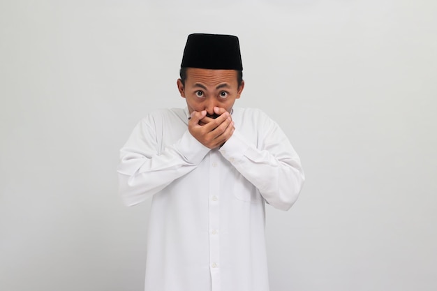 Der verlegene junge indonesische Mann ist schockiert und bedeckt seinen Mund isoliert auf weißem Hintergrund