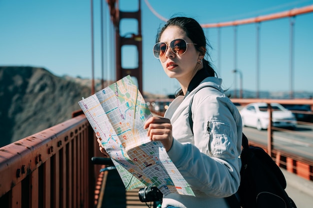 Der verlorene asiatische Mädchenreisende hält eine Karte und blickt mit einem verwirrten Ausdruck auf der Golden Gate Bridge in San Francisco, USA, in die Ferne.