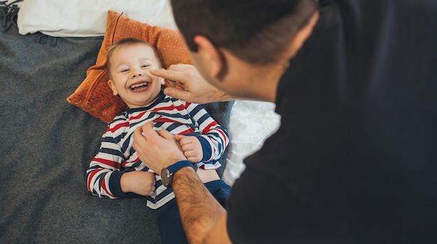 Der verspielte Vater kitzelt seinen kleinen Sohn, der auf dem Sofa liegt und freudig lächelt