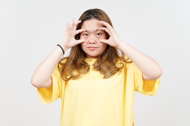 Der Versuch, die Augen mit den Fingern einer schönen asiatischen Frau zu öffnen, die ein gelbes T-Shirt isoliert auf Weiß trägt