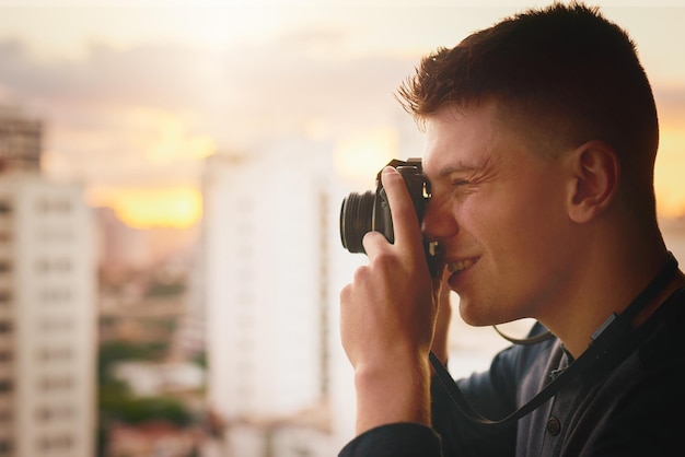 Der versuch, die perfekte aufnahme von diesem perfekten ort aus zu machen zugeschnittene aufnahme eines jungen mannes, der draußen mit einer kamera fotos von der stadt macht