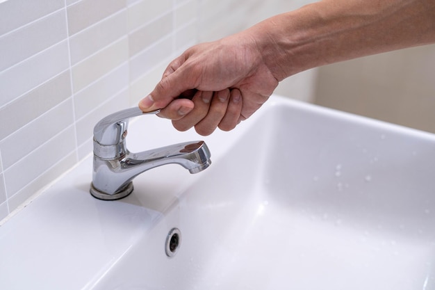 Der Wasserhahn im Badezimmer mit fließendem Wasser Mann schaltet das Wasser immer wieder ab, um Wasserenergie zu sparen und die Umwelt zu schützen Wasser sparen Konzept