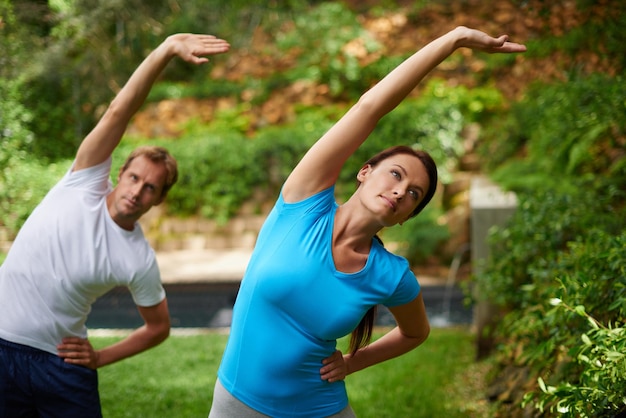 Der Weg zur Flexibilität Aufnahme eines Mannes und einer Frau, die in einem Outdoor-Yoga-Kurs eine Seitendehnung ausführen