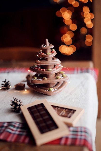 Foto der weihnachtsbaum, der von der natürlichen schokolade hergestellt wird, steht auf der festlichen tabelle vor dem hintergrund der lichter, gemütliche hauptatmosphäre