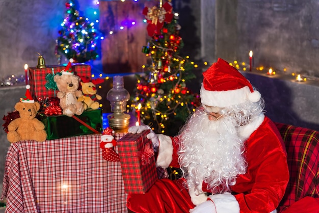 Der Weihnachtsmann hält eine Geschenkbox zu Hause. Setzen Sie sich auf einen Stuhl und denken Sie über den Plan nach, eine Geschenkbox für Kinder zu versenden