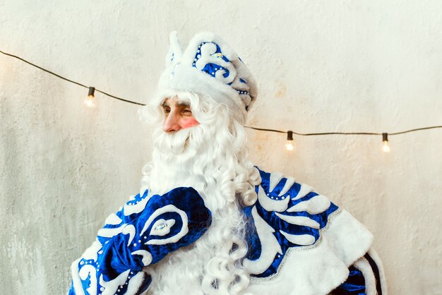 Der Weihnachtsmann in einem blauen Pelzmantel schaut aus dem Fenster, denkt nach und berührt seinen Bart.