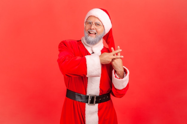 Der Weihnachtsmann kreuzt die Finger, um ein Hashtag-Zeichen zu machen und mit einem zahnigen Lächeln in die Kamera zu schauen.