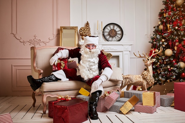 Der Weihnachtsmann legte sich mit ein paar Geschenken in der Nähe des Kamins und des Weihnachtsbaums auf das Sofa