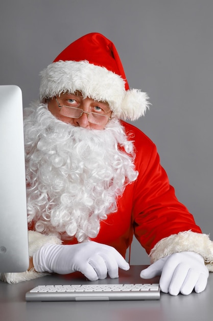 Der Weihnachtsmann liest Kinderbriefe und schreibt ihnen mit einem Laptop Antworten.