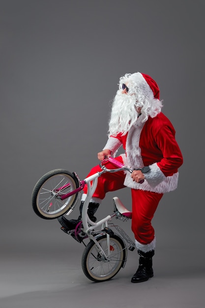 Der Weihnachtsmann mit Sonnenbrille und Kopfhörern stellt das Fahrrad auf das Hinterrad auf weißem Hintergrund. .