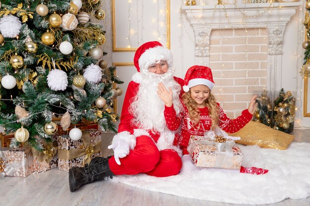 Der Weihnachtsmann schenkt einem kleinen Mädchen am Weihnachtsbaum ein Geschenk