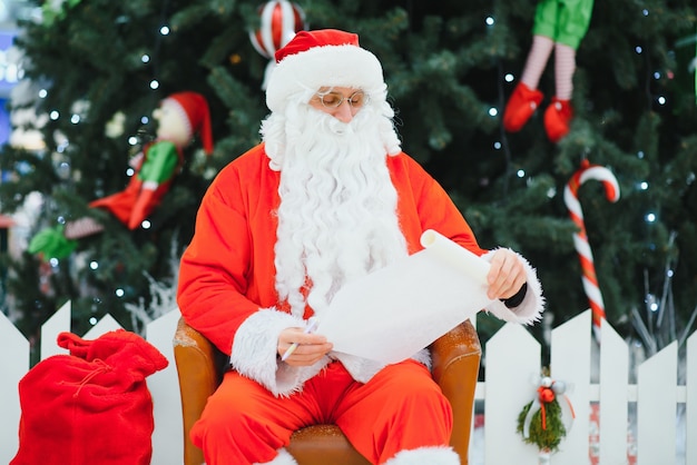 Der Weihnachtsmann sitzt auf dem Hintergrund des Weihnachtsbaums in der Lobby des modernen Einkaufszentrums. Bokeh-Grundhintergrund für Design.