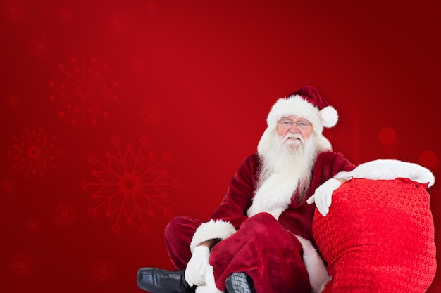 Der Weihnachtsmann sitzt neben seiner Tasche vor rotem Hintergrund