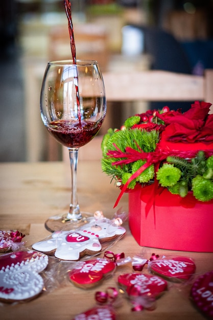 Der Wein wird in ein Glas gegossen. Roter Blumenstrauß zum Valentinstag