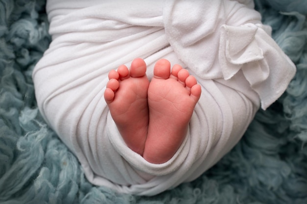 Der winzige Fuß eines Neugeborenen Weiche Füße eines Neugeborenen in einer weißen Decke und auf blauem Hintergrund Nahaufnahme der Zehen, Fersen und Füße eines neugeborenen Babys Studio Makrofotografie Woman39s Glück