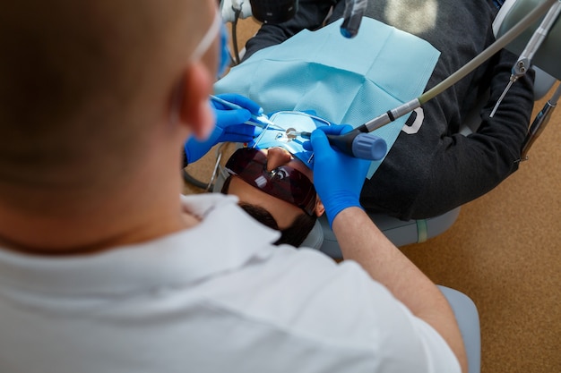 Foto der zahnarzt behandelt die zähne seines patienten mit einem mikroskop. der zahnarzt behandelt den mund des patienten. zahnpflege. foto in hoher qualität