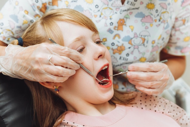 Der Zahnarzt führt ein Untersuchungsverfahren auf einem netten kleinen Mädchen durch Kleines Mädchen, das in der Zahnarztpraxis sitzt