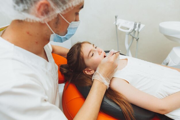 Foto der zahnarzt führt ein untersuchungsverfahren auf einem netten kleinen mädchen durch kleines mädchen, das in der zahnarztpraxis sitzt