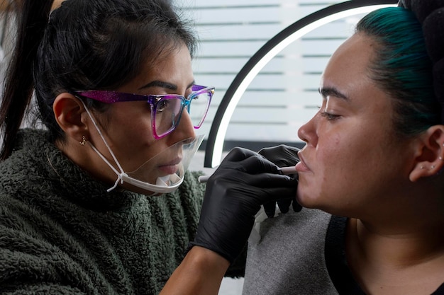 Dermatologista estilizando os lábios de uma mulher antes de tatuar maquiagem permanente nos lábios