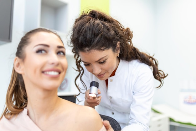 Foto dermatologista feminina examinando cuidadosamente a pele de uma paciente do sexo feminino usando um dermatoscópio procurando sinais de câncer de pele dermatologista examinando marca de nascença de pacientes com lupa na clínica