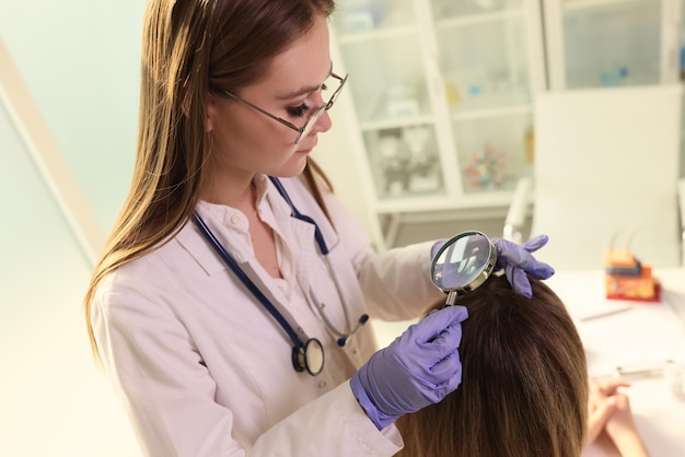 Foto dermatologista feminino verifica a saúde do cabelo e couro cabeludo de seu paciente com lupa