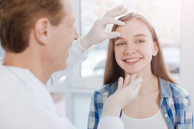 Un dermatólogo calificado, amable y atento que disfruta de las horas de trabajo en el hospital y se sienta en el gabinete mientras examina la piel del paciente