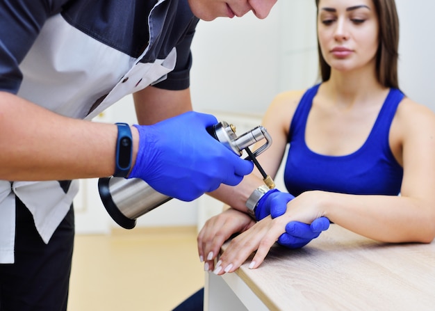 Un dermatólogo examina a una mujer y sostiene un dispositivo especial: un criodestructor.