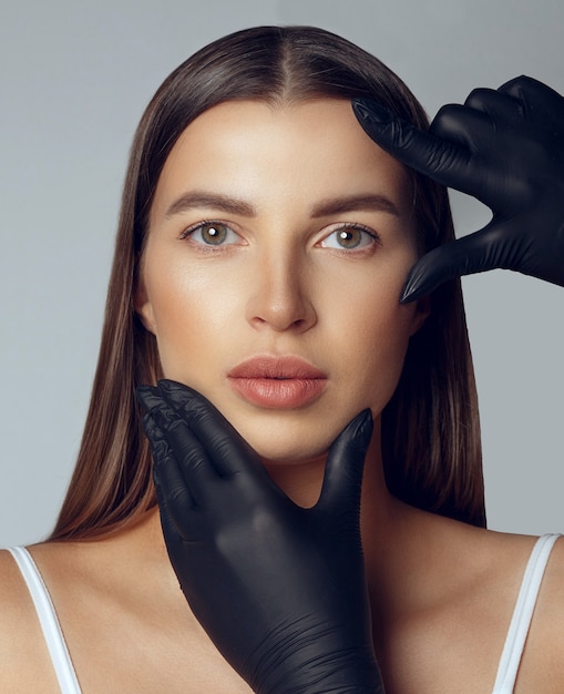 Dermatólogo en guantes negros comprobando el rostro de la mujer antes de la cirugía plástica