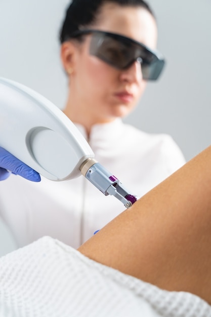 Foto dermatólogo profesional serio centrado en gafas de seguridad apretando la piel suelta en la cadera de una mujer