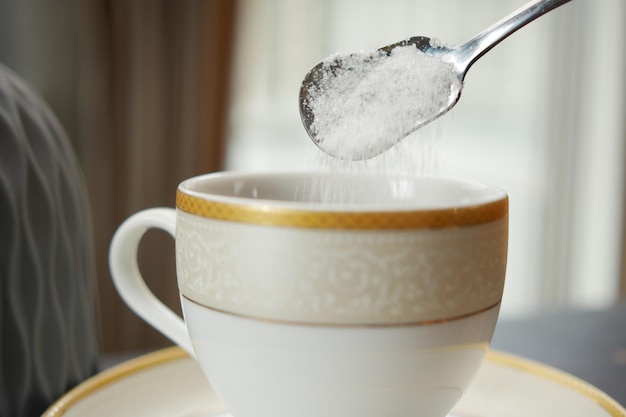 Derramando açúcar branco em uma xícara de café
