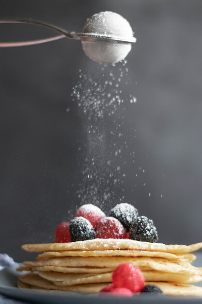 Derramando açúcar sobre crepes caseiros na mesa, fotografia de comida escura