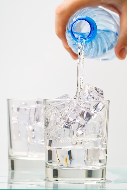 Derramando água potável de uma garrafa de plástico azul em um copo com fundo azul