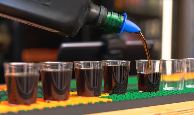 Derramando bebida alcoólica forte e escura em copos pequenos em fotos de bar