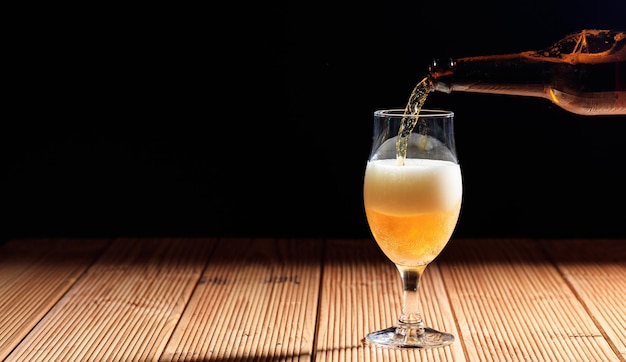 Derramando cerveja em um copo sobre uma mesa de madeira fundo escuro